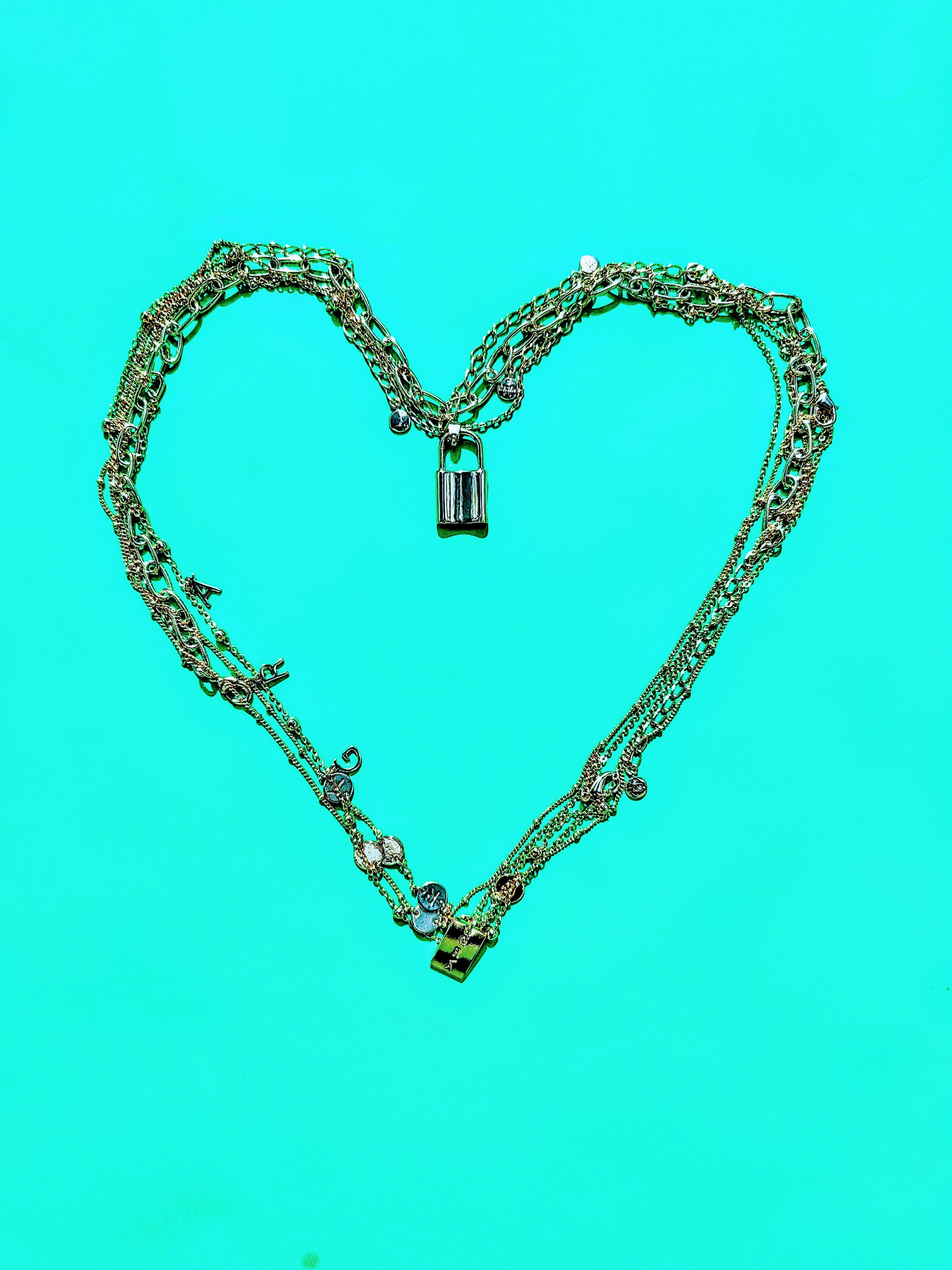 Silver chain necklace with multiple links and a small padlock charm on a bright turquoise background