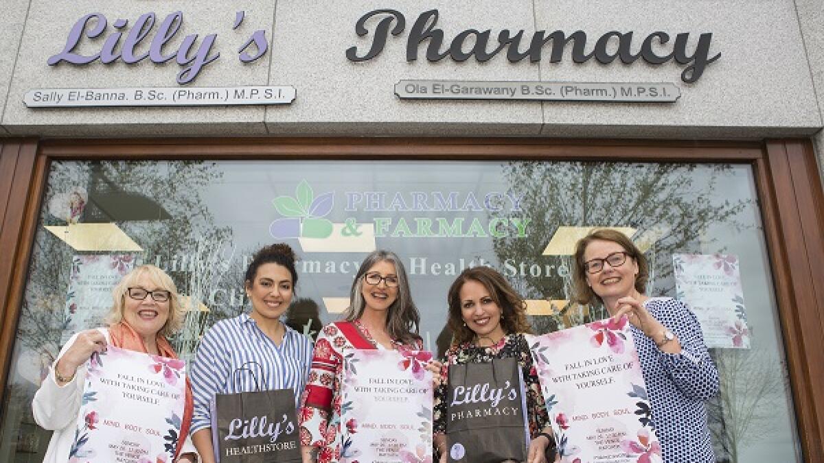 Group outside pharmacy storefront holding branded shopping bags, with Pharmacy and Pharmacy Health Store signage