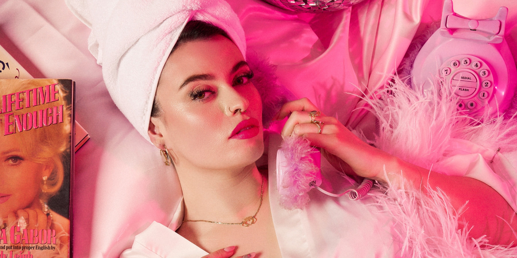 Woman in a white hat and jewellery reclining with a pink feather boa and a vintage rotary phone