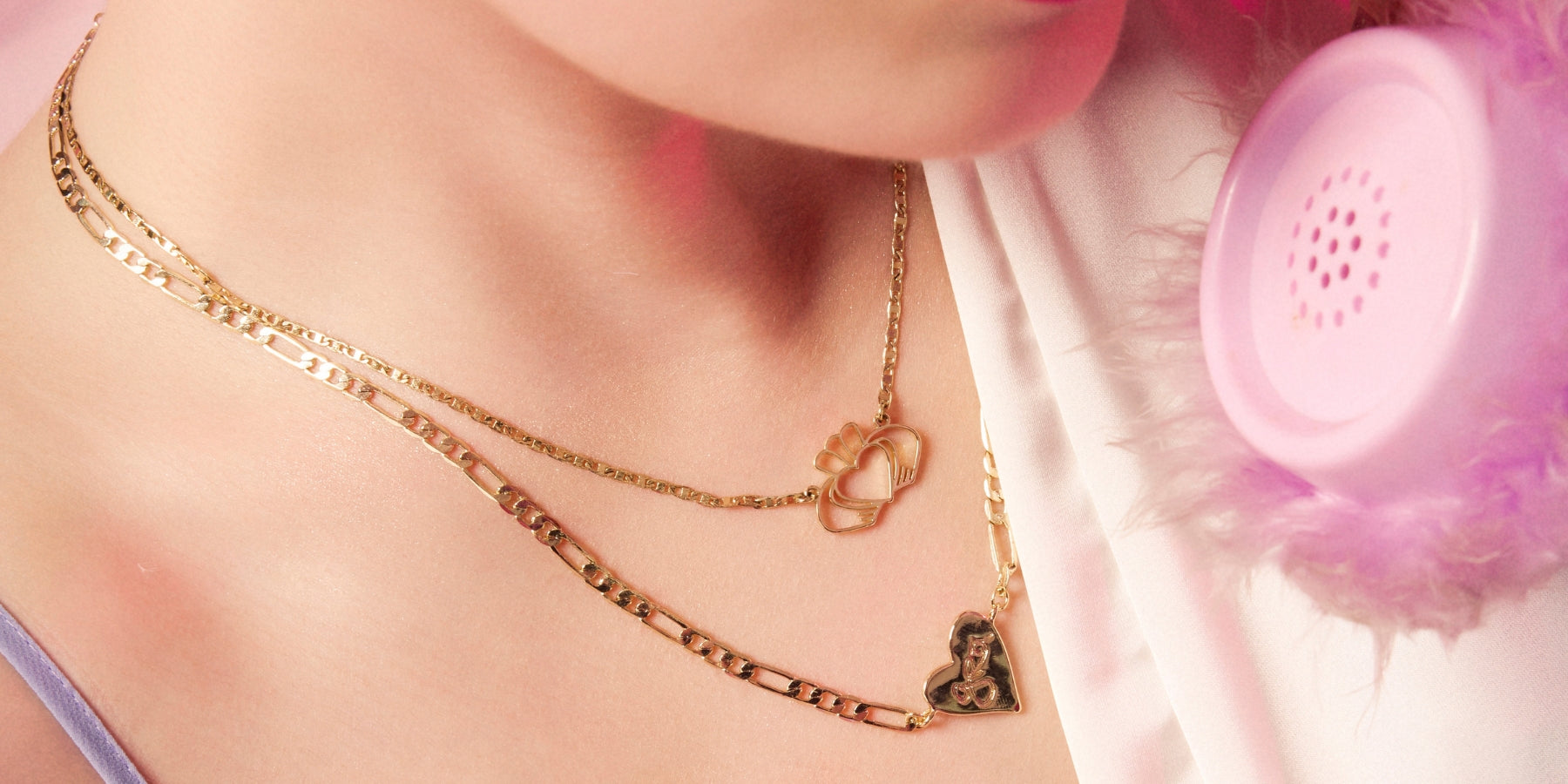 Gold layered necklace with heart and bear charms on a pink fabric background with a purple bracelet