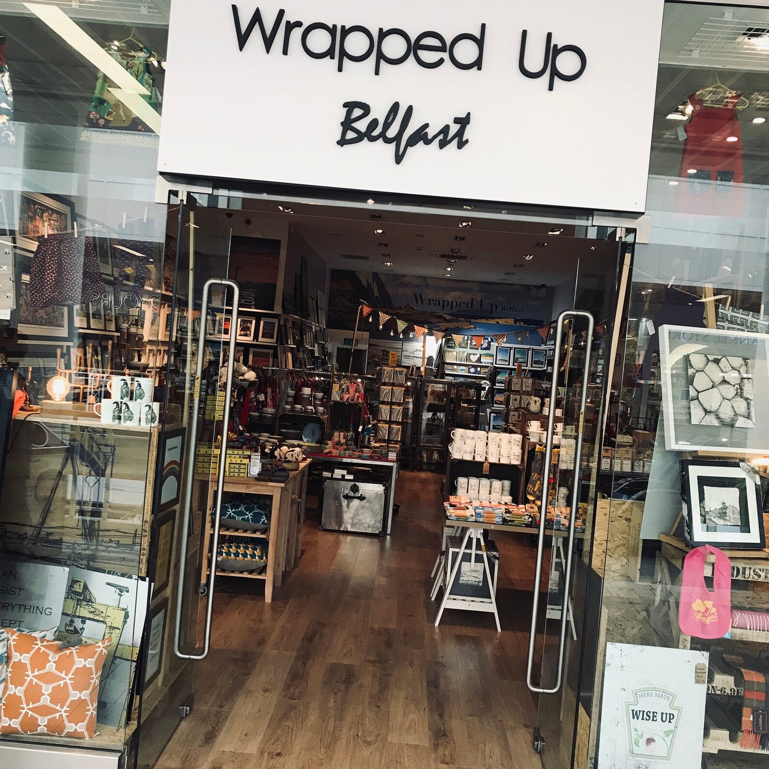 Shop entrance with large sign reading Wrapped Up Belfast, shelves of gifts and mugs inside