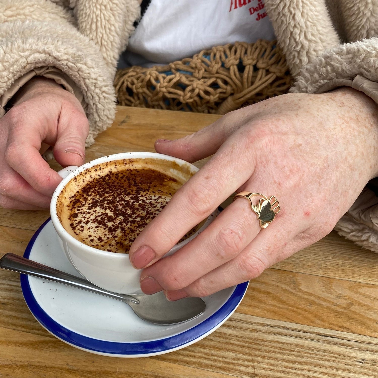 Model wearing Have My Heart Gold Claddagh Ring about to have a cappuccino 